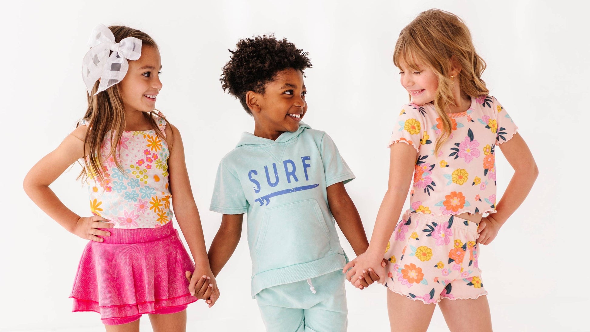Three children wearing colorful, quality outfits standing together on a white background